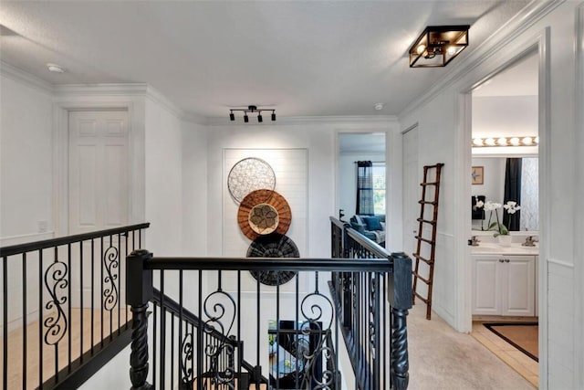 hallway featuring an upstairs landing, track lighting, light colored carpet, and crown molding