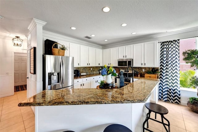 kitchen featuring backsplash, white cabinetry, dark stone counters, appliances with stainless steel finishes, and light tile patterned floors