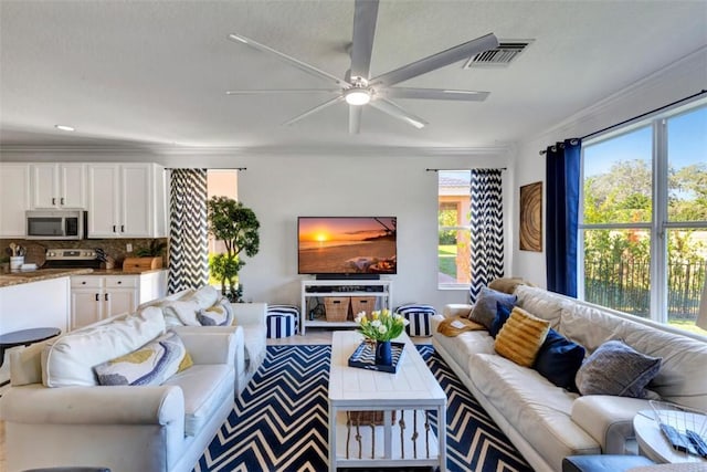 living area featuring ceiling fan, visible vents, a wealth of natural light, and ornamental molding