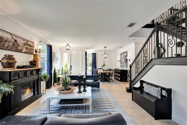 living room featuring visible vents, crown molding, stairway, light tile patterned flooring, and a glass covered fireplace