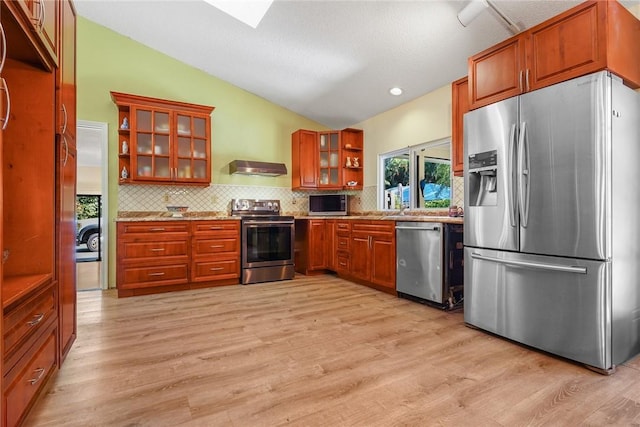 kitchen featuring tasteful backsplash, lofted ceiling with skylight, appliances with stainless steel finishes, and light hardwood / wood-style floors