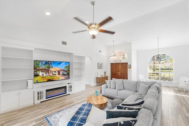 living room with built in shelves, lofted ceiling, ceiling fan with notable chandelier, and light hardwood / wood-style flooring