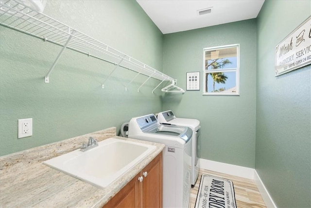 laundry room featuring cabinets, sink, washing machine and dryer, and light hardwood / wood-style flooring