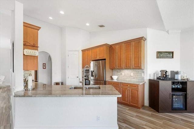 kitchen with stainless steel refrigerator with ice dispenser, lofted ceiling, light stone counters, and kitchen peninsula