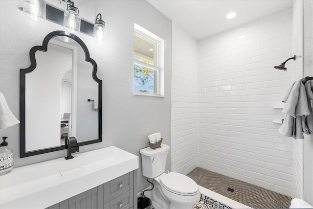 bathroom featuring vanity, a tile shower, and toilet