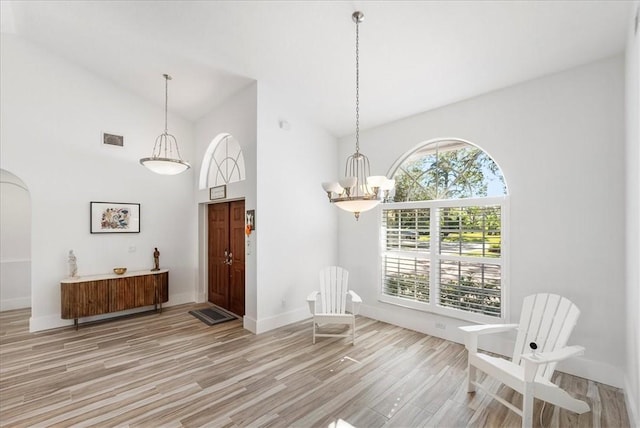 interior space with high vaulted ceiling, a notable chandelier, and light hardwood / wood-style floors