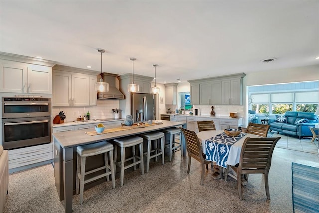 kitchen featuring decorative backsplash, appliances with stainless steel finishes, wall chimney range hood, pendant lighting, and a center island