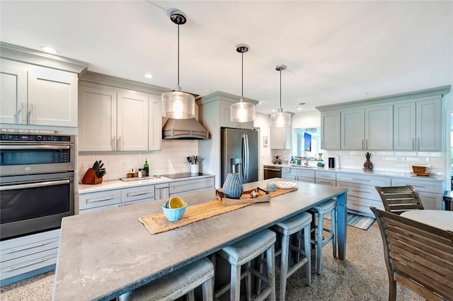 kitchen with pendant lighting, premium range hood, decorative backsplash, appliances with stainless steel finishes, and a kitchen island