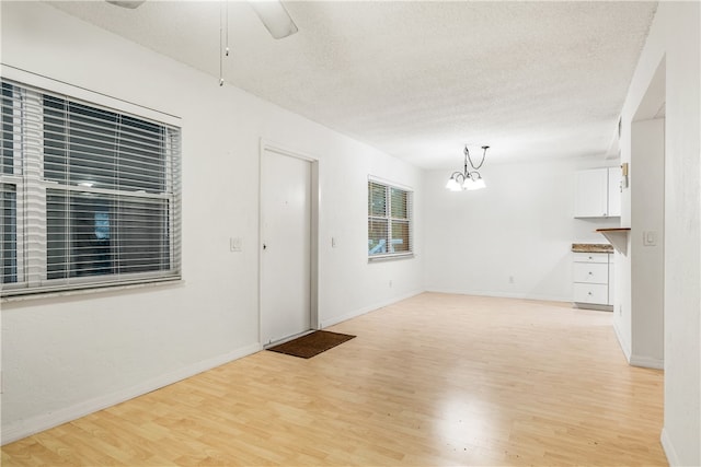 empty room with ceiling fan with notable chandelier, light hardwood / wood-style floors, and a textured ceiling