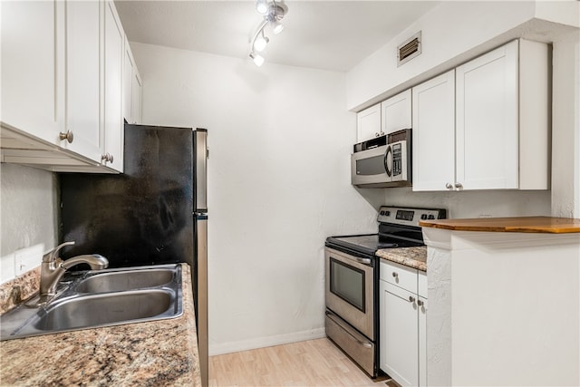 kitchen with white cabinetry, sink, light stone counters, appliances with stainless steel finishes, and light wood-type flooring