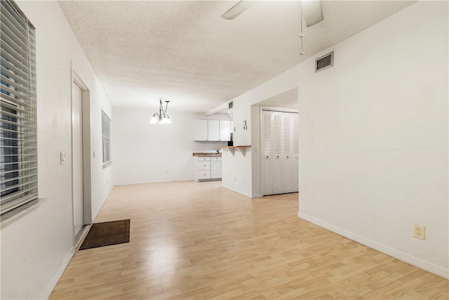 unfurnished living room with ceiling fan with notable chandelier, a textured ceiling, and light wood-type flooring