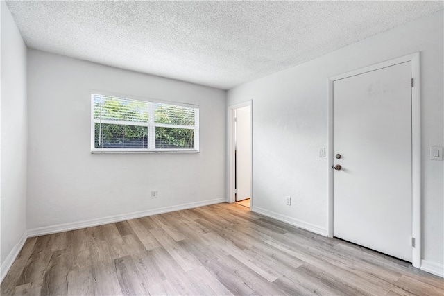 unfurnished room with light wood-type flooring and a textured ceiling