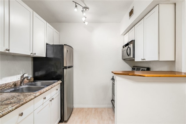 kitchen featuring dark stone counters, sink, white cabinetry, light wood-type flooring, and appliances with stainless steel finishes