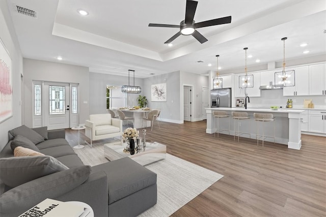 living room with a raised ceiling, ceiling fan, and light hardwood / wood-style flooring