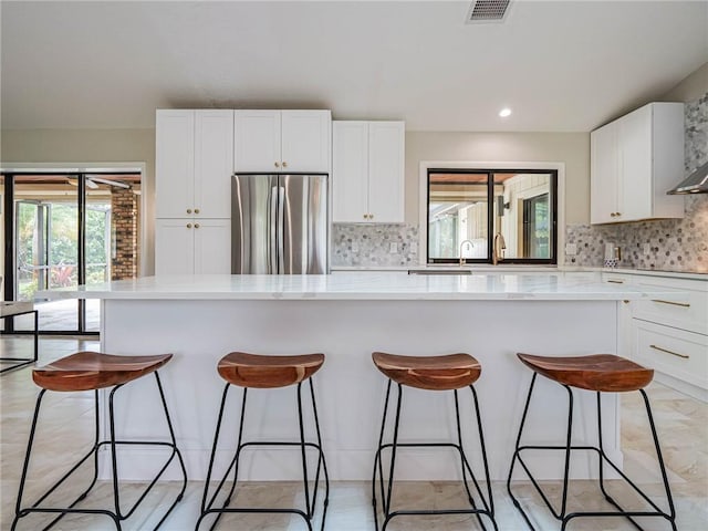 kitchen with a center island, white cabinets, stainless steel refrigerator, and decorative backsplash