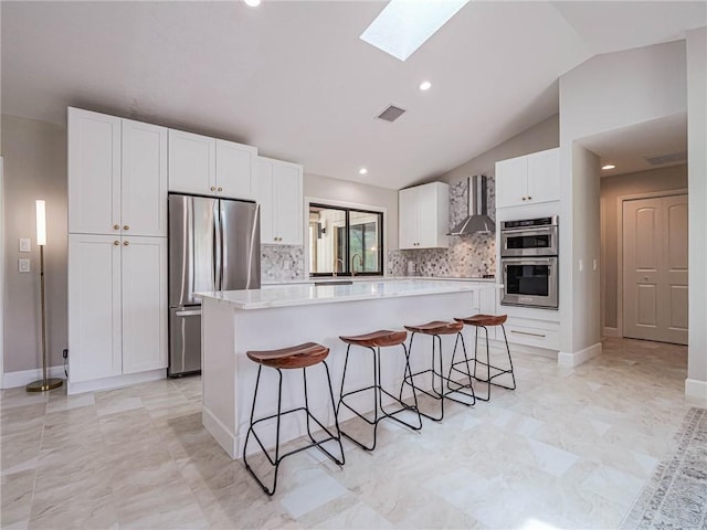 kitchen featuring a breakfast bar, white cabinetry, a kitchen island, stainless steel appliances, and wall chimney range hood