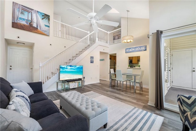 living room featuring high vaulted ceiling, stairway, a ceiling fan, wood finished floors, and baseboards