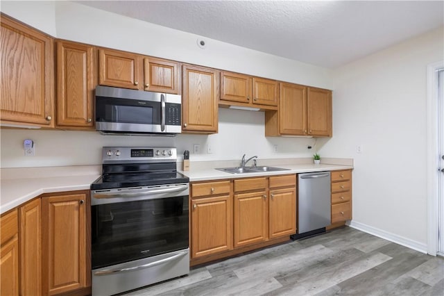 kitchen featuring appliances with stainless steel finishes, a sink, light wood-type flooring, light countertops, and brown cabinetry