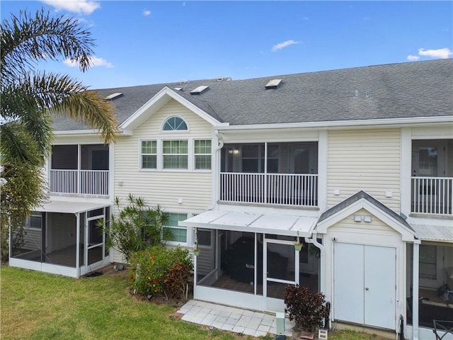 rear view of property featuring a sunroom, a shingled roof, and a lawn