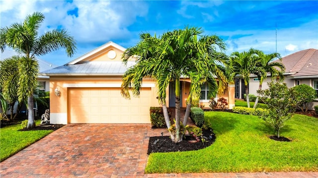 single story home with decorative driveway, stucco siding, metal roof, a garage, and a front lawn