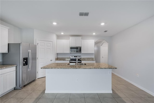 kitchen with appliances with stainless steel finishes, sink, light stone countertops, and an island with sink