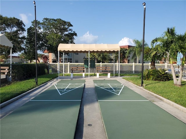 view of property's community featuring fence, a lawn, and shuffleboard