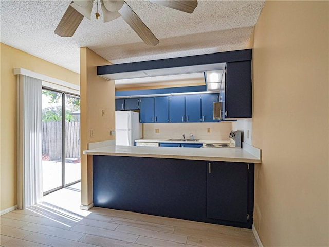 kitchen featuring blue cabinetry, range, a textured ceiling, light wood-type flooring, and white refrigerator