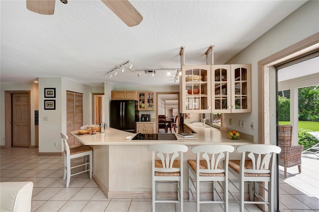 kitchen featuring a breakfast bar, black refrigerator, ceiling fan, light tile patterned floors, and kitchen peninsula