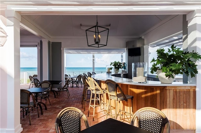 dining space featuring a water view, brick floor, a chandelier, and crown molding