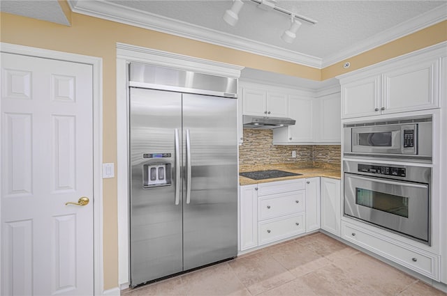 kitchen featuring backsplash, ornamental molding, white cabinets, built in appliances, and under cabinet range hood