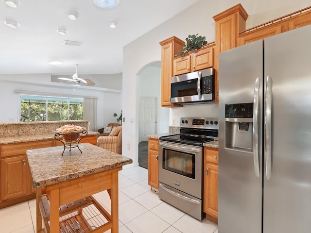 kitchen with lofted ceiling, ceiling fan, light tile patterned flooring, appliances with stainless steel finishes, and light stone counters