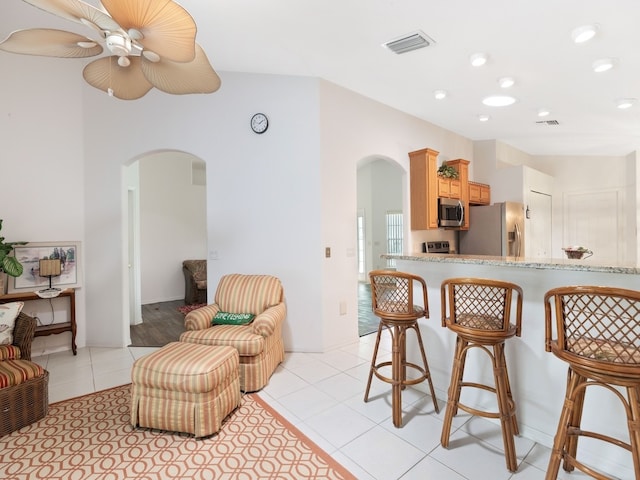 kitchen with a kitchen bar, stainless steel appliances, light brown cabinetry, ceiling fan, and light tile patterned floors