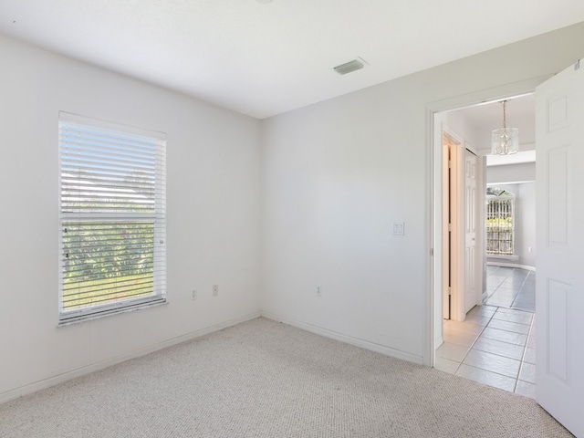 carpeted spare room featuring a healthy amount of sunlight and a notable chandelier