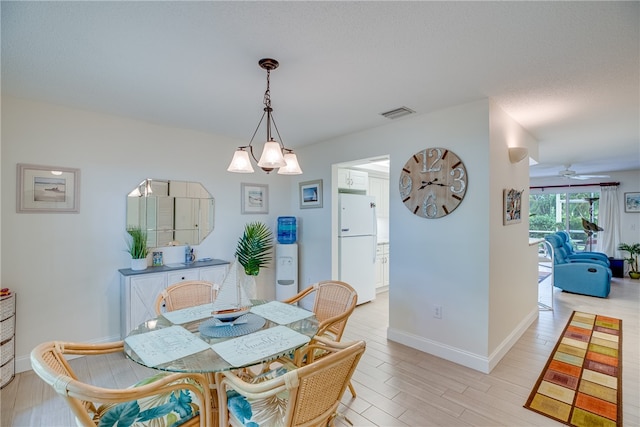 dining space with ceiling fan with notable chandelier and light hardwood / wood-style flooring