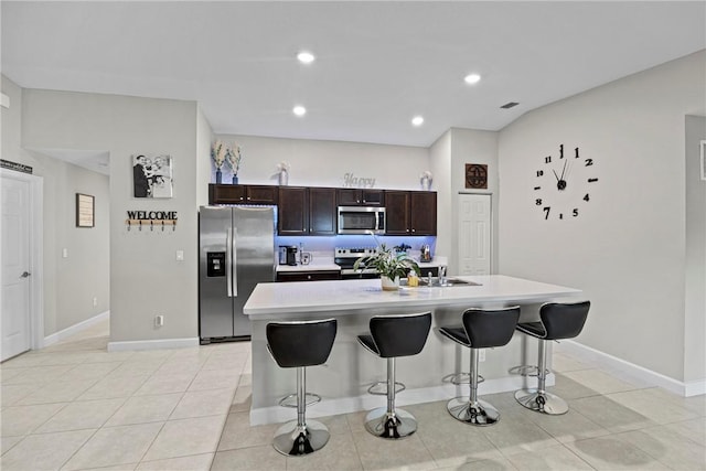 kitchen with a breakfast bar, appliances with stainless steel finishes, dark brown cabinets, and an island with sink