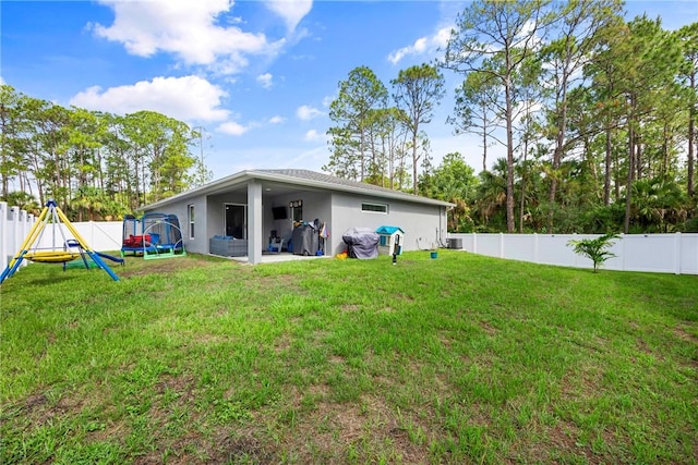 back of house featuring a playground, a patio, a trampoline, and a lawn