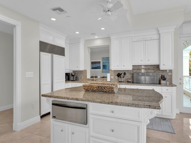 kitchen with light stone counters, a kitchen island, paneled built in fridge, decorative backsplash, and white cabinets