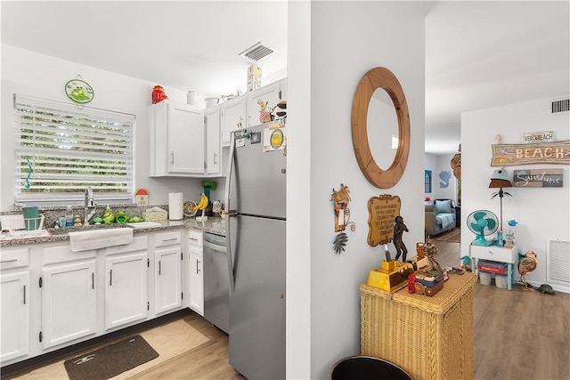 kitchen with sink, appliances with stainless steel finishes, light stone countertops, white cabinets, and light wood-type flooring