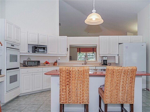 kitchen featuring a kitchen bar, hanging light fixtures, sink, white cabinets, and white appliances