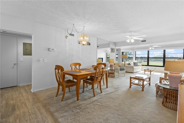 dining area with electric panel, visible vents, wood finished floors, a textured ceiling, and ceiling fan with notable chandelier