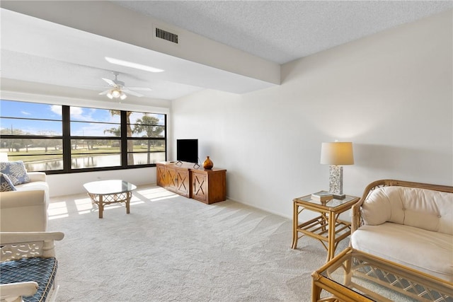 living area featuring carpet, visible vents, ceiling fan, and a textured ceiling