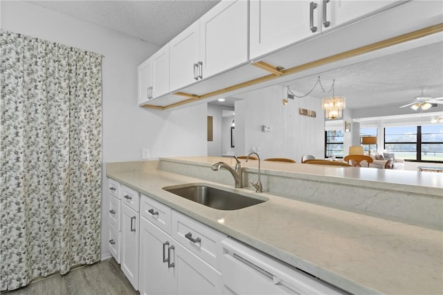 kitchen featuring light wood-style floors, a ceiling fan, white cabinets, a sink, and a textured ceiling