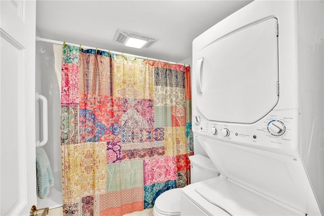 bathroom featuring stacked washer / drying machine, curtained shower, and toilet