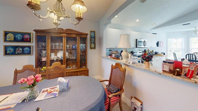 dining space with ceiling fan with notable chandelier, a textured ceiling, and vaulted ceiling