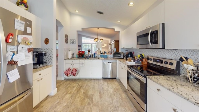 kitchen featuring light wood-type flooring, appliances with stainless steel finishes, decorative light fixtures, white cabinets, and lofted ceiling