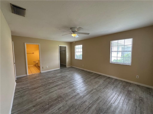 unfurnished bedroom with dark hardwood / wood-style flooring, a walk in closet, ceiling fan, ensuite bath, and a closet