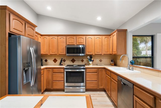 kitchen with appliances with stainless steel finishes, tasteful backsplash, lofted ceiling, sink, and light hardwood / wood-style floors