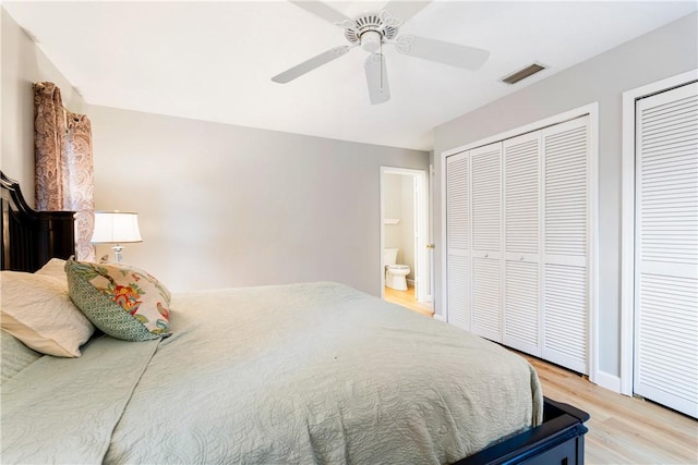 bedroom featuring multiple closets, ensuite bathroom, light wood-type flooring, and ceiling fan