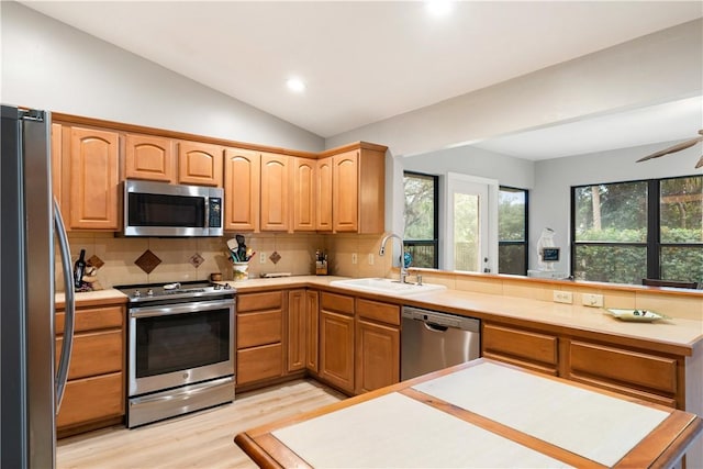 kitchen with lofted ceiling, sink, light hardwood / wood-style flooring, backsplash, and stainless steel appliances