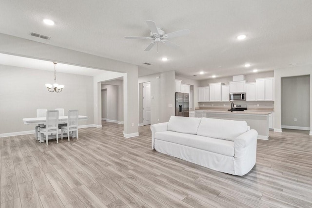 living room with ceiling fan with notable chandelier and light wood-type flooring